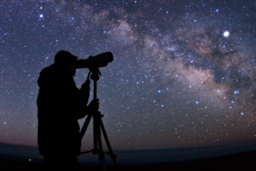 Silhouette of a person observing the Milky Way through a telescope.