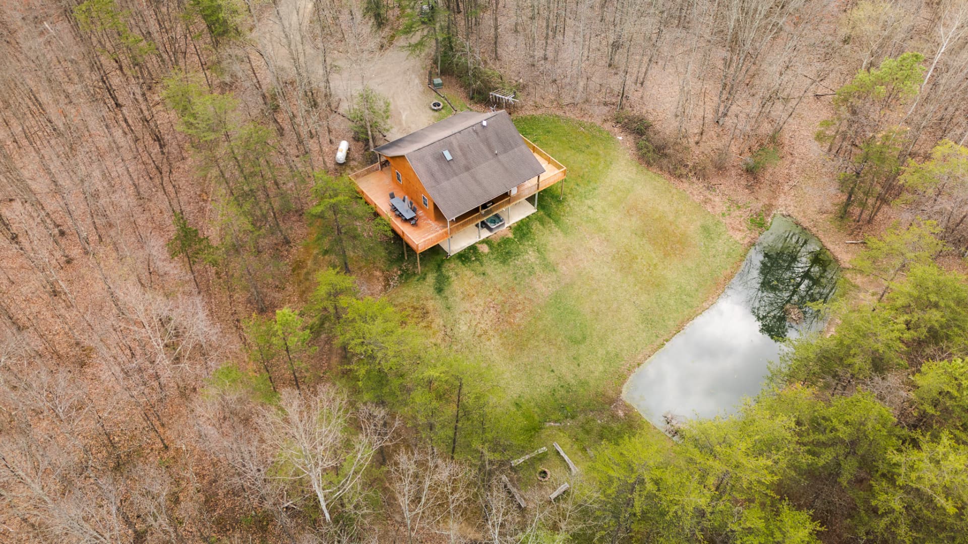 Aerial view of a house surrounded by trees with a small pond nearby.