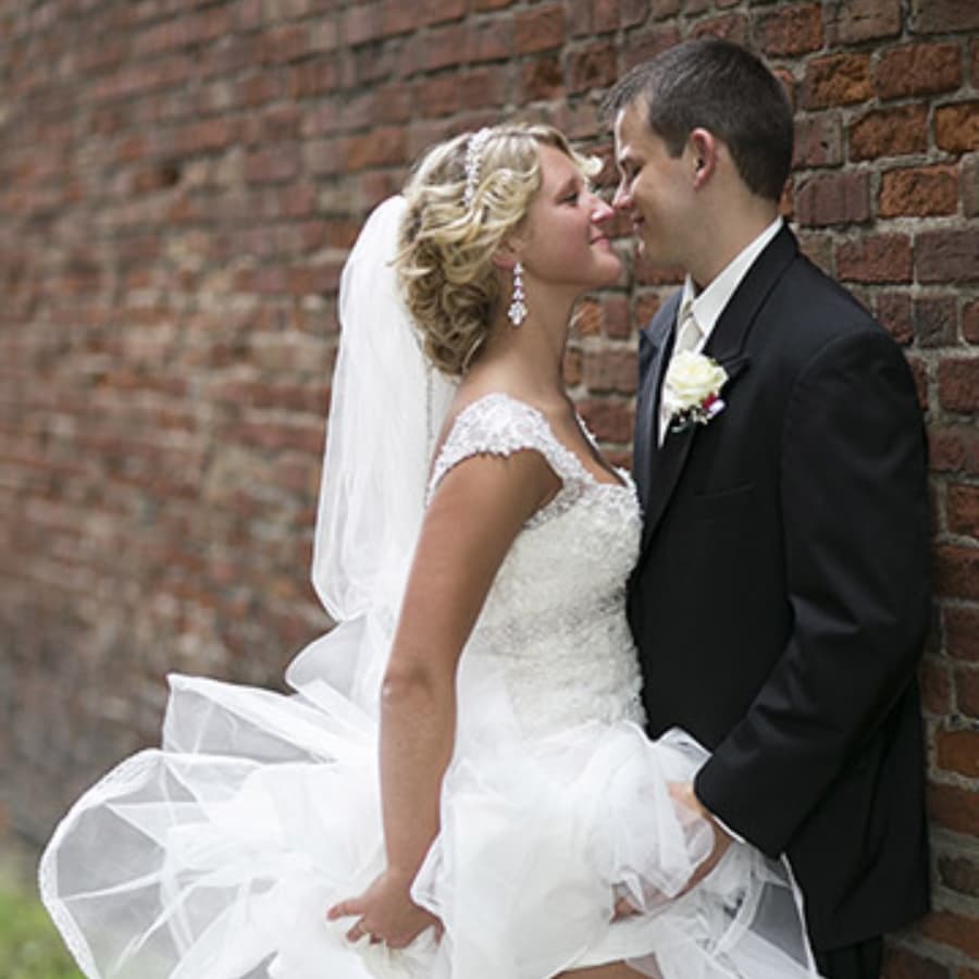 A bride and groom share a loving moment in front of a brick wall.