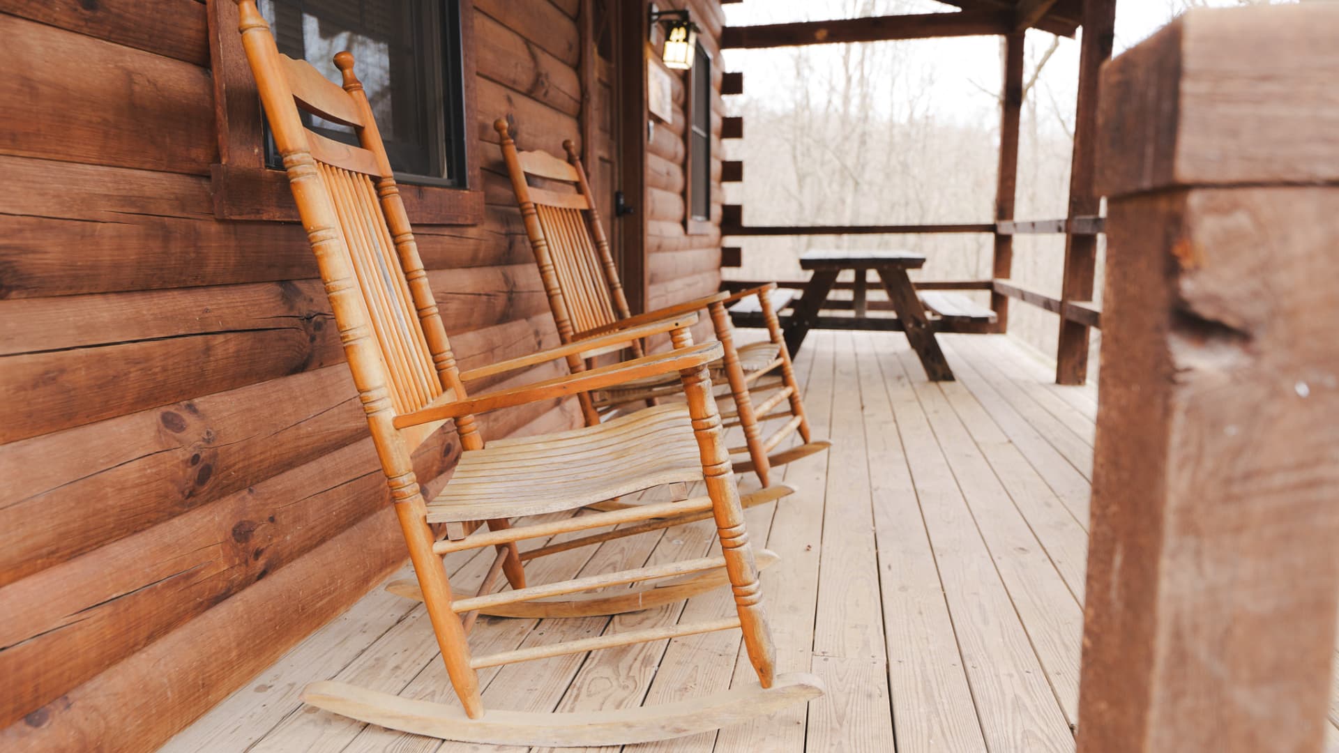 Two wooden rocking chairs on a log cabin porch overlooking a wooded area.